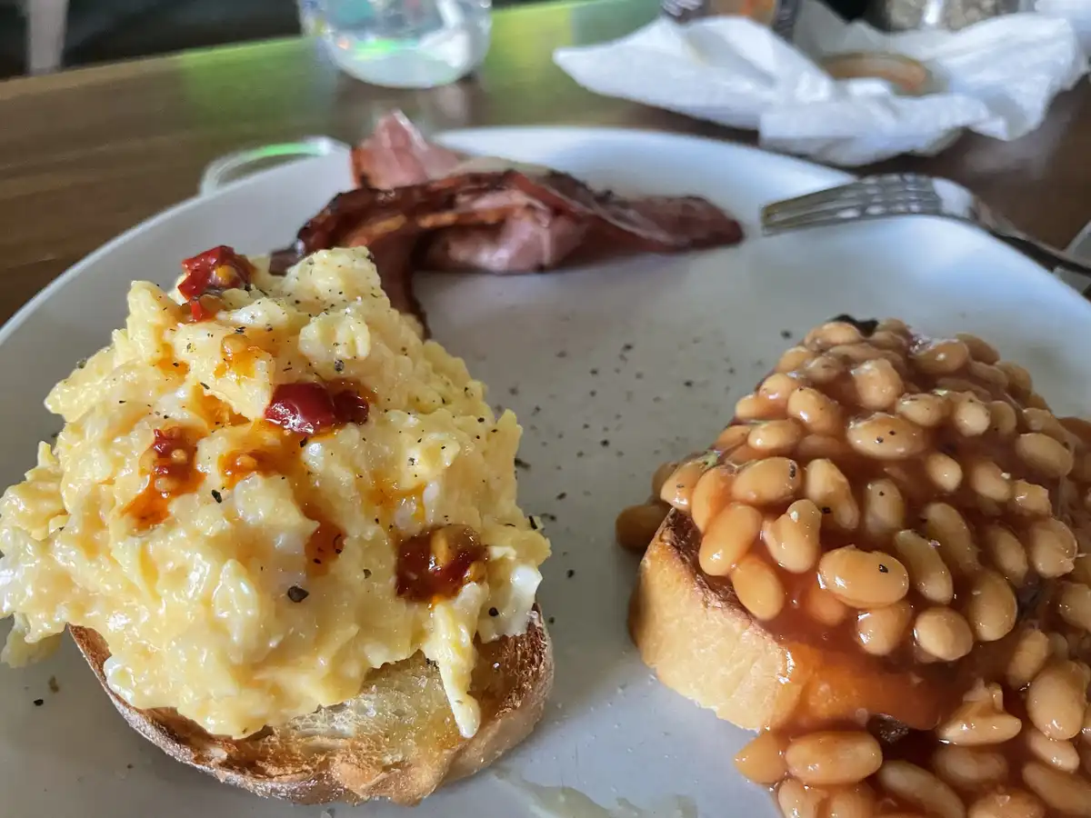 A close-up photo of a plate of breakfast food including scrambled eggs with red pepper flakes on toast, baked beans on…