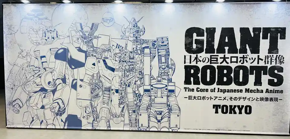 A large exhibition banner displays a detailed blue-and-white line art illustration of numerous giant robots from Japanese…