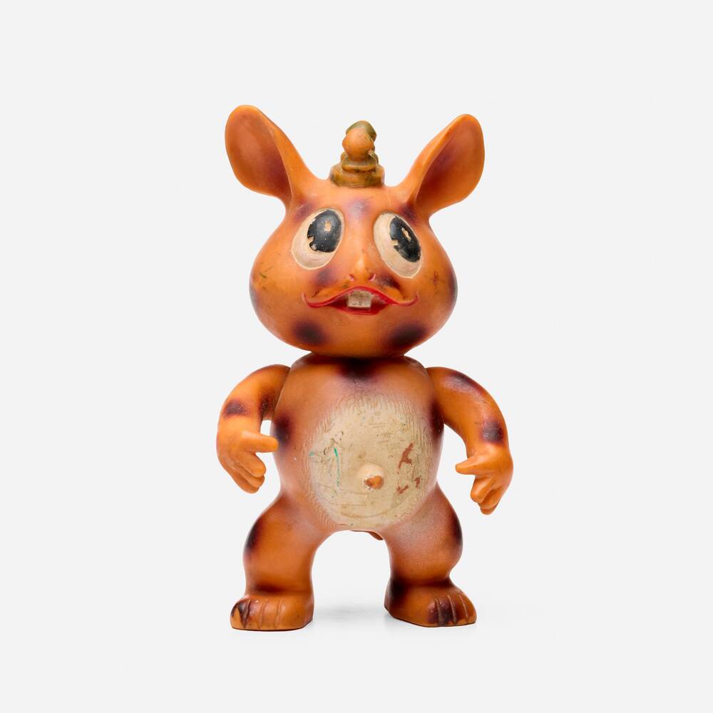 A vintage, orange-brown plastic toy figure resembling a rabbit with large, round eyes, a painted mustache, and a small…