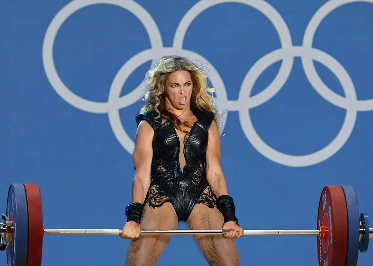 A woman with blonde hair, wearing a black lace bodysuit and fishnet stockings, is mid-lift holding a barbell with red and…