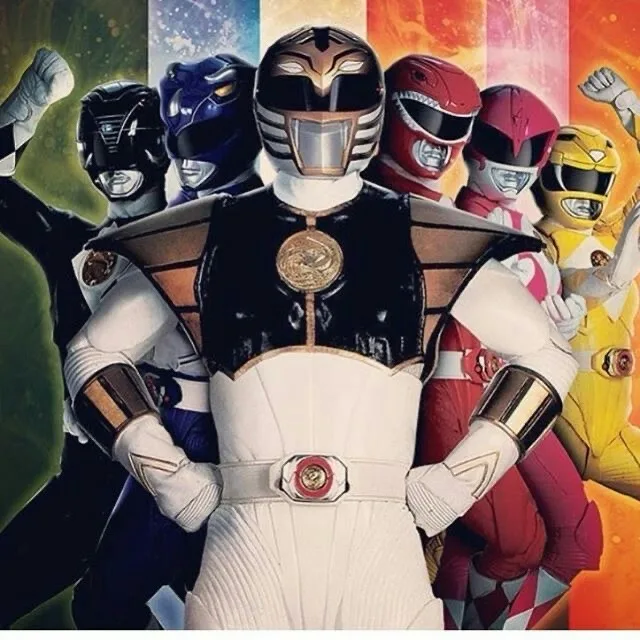 A group of Power Rangers stand together, with the Black Ranger in the center, arms crossed, while the other Rangers (Black…