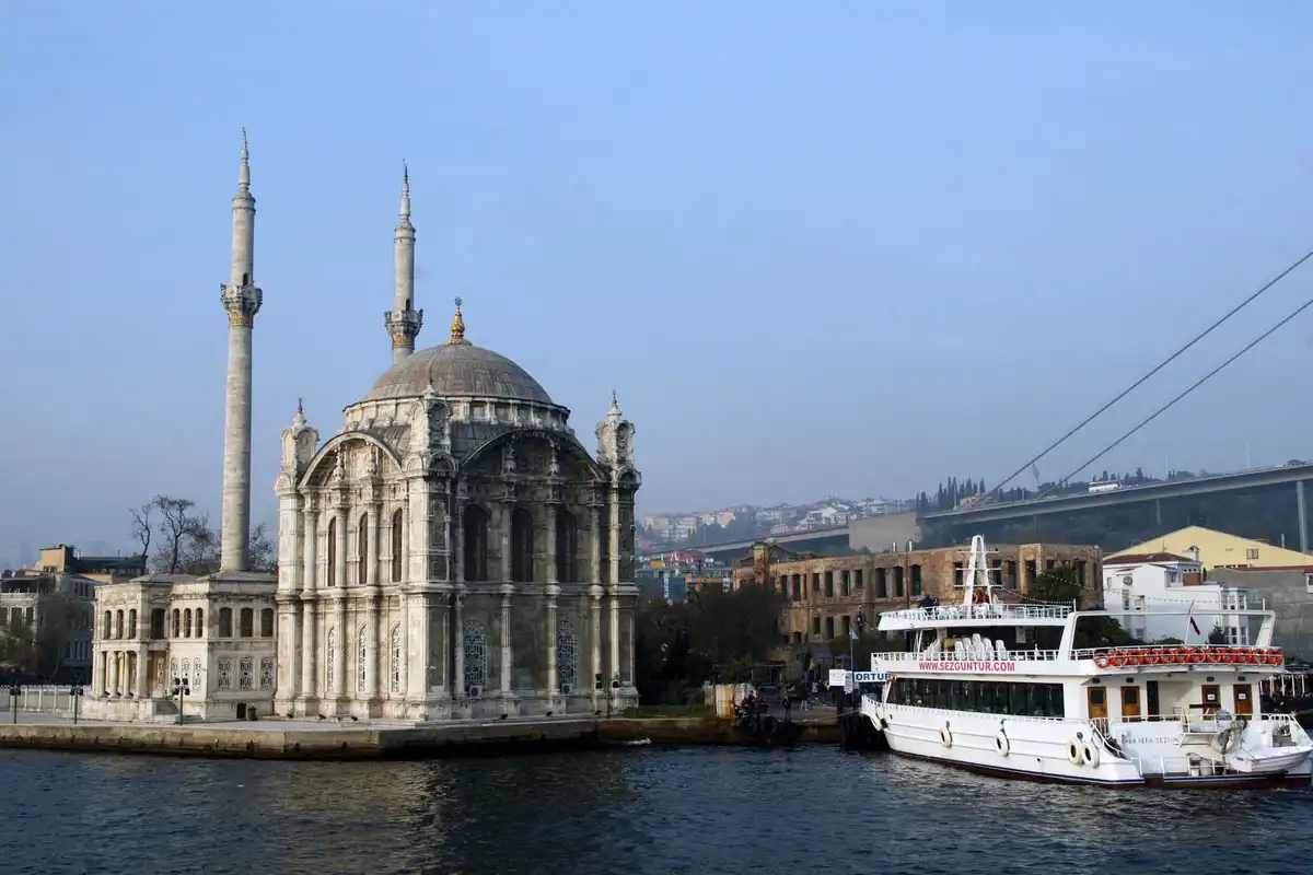 A scenic photo of the Ortaköy Mosque in Istanbul, featuring its prominent dome and two minarets beside a body of water, with…