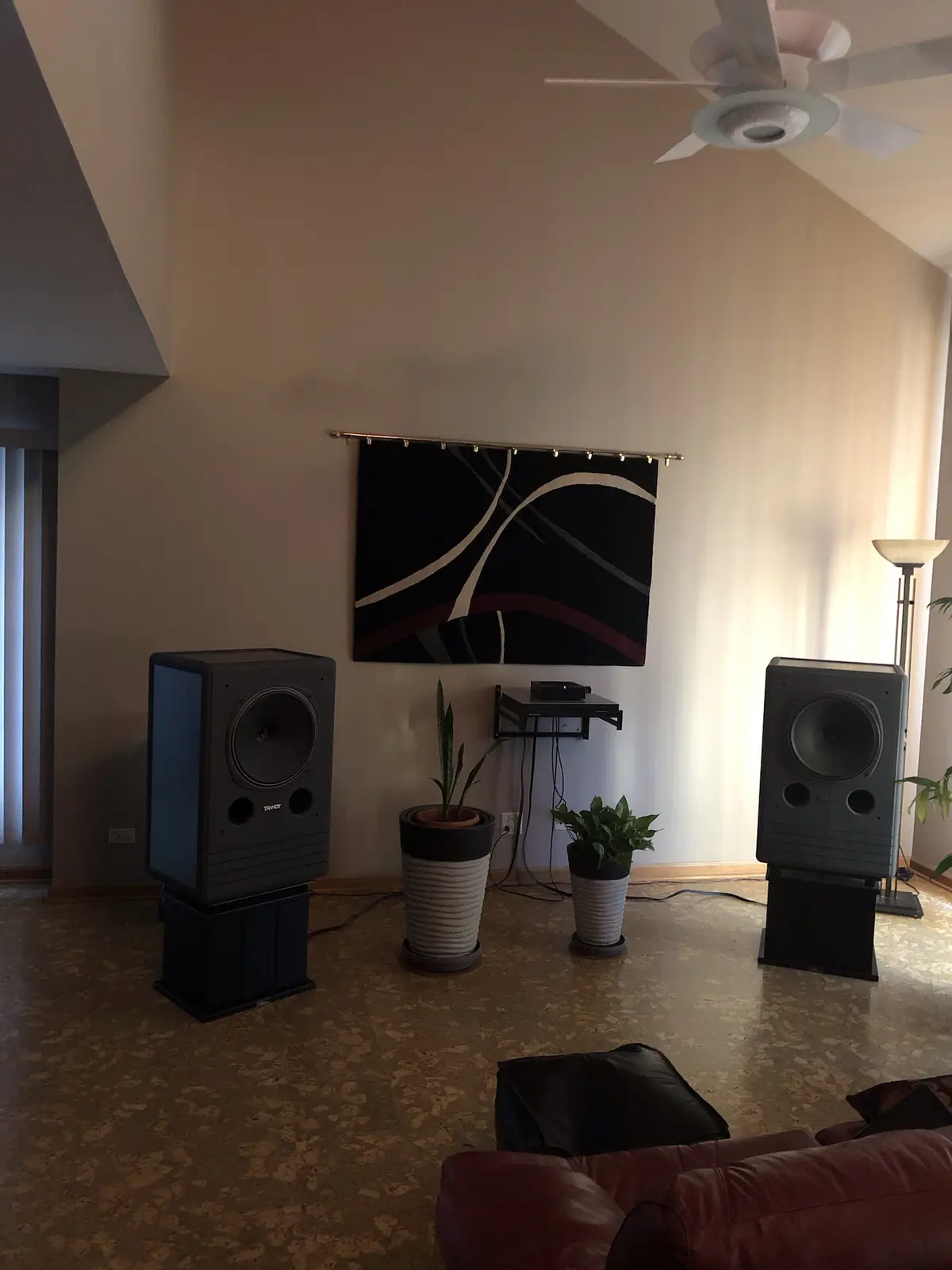 A living room with two large floor-standing speakers on stands, positioned symmetrically on either side of a wall with…