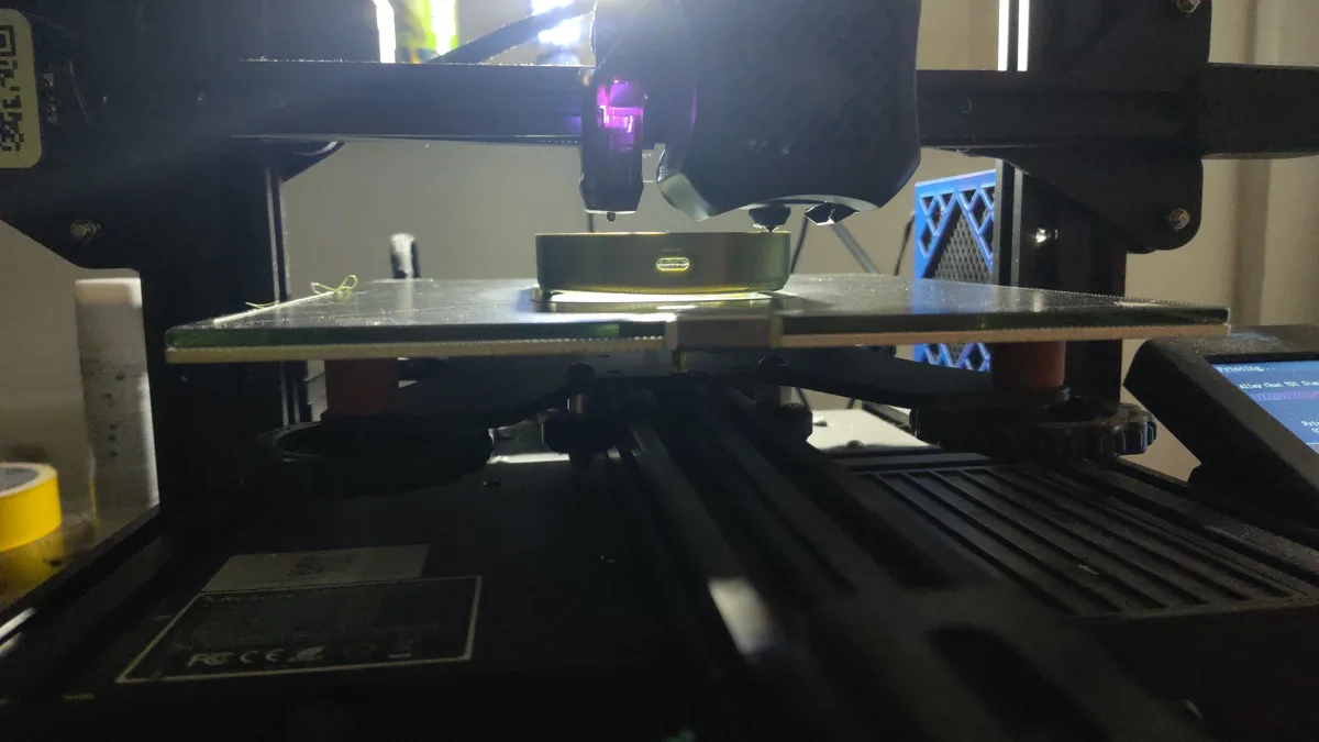 A 3d printer is actively printing a small, rectangular object that resembles a phone charger with a USB-C port on its…