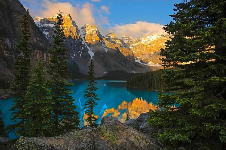 A breathtaking landscape photo of a turquoise lake reflecting golden, snow-capped mountains under a partly cloudy sky…