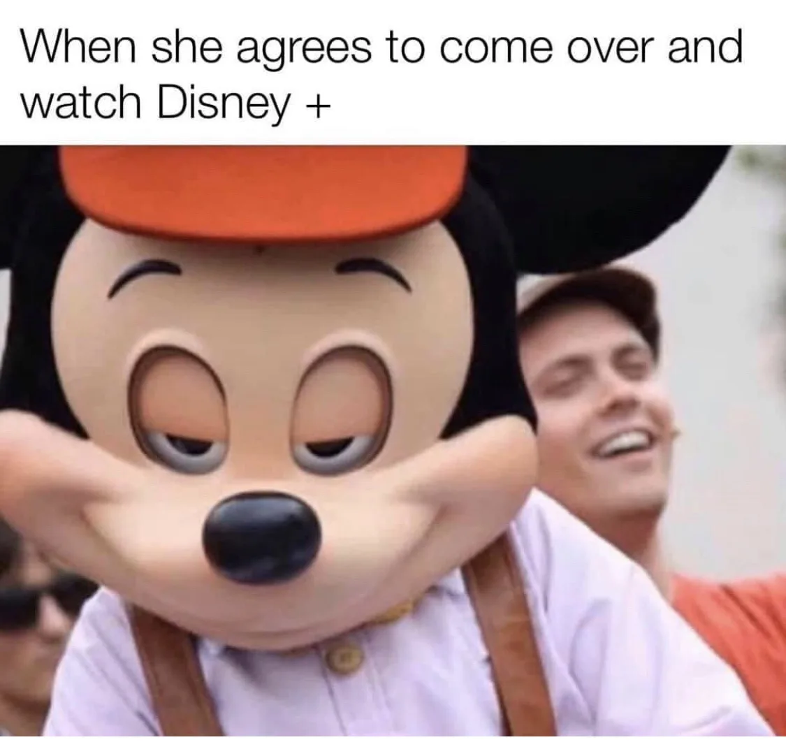 A person in a large Mickey Mouse costume with a smug, self-satisfied expression, eyes half-closed and hands on cheeks, while…