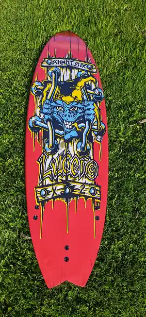 A red surfboard with a vibrant, dripping graffiti-style graphic of a blue, angry, skull-faced creature wearing a yellow…