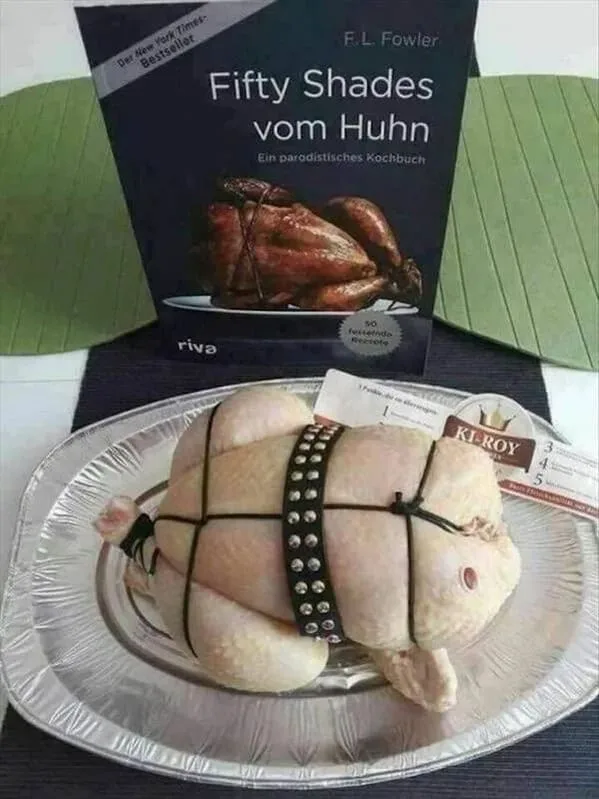 A raw chicken on a silver platter is strapped with black bands and a studded belt, mimicking a BDSM scene. Behind it stands…