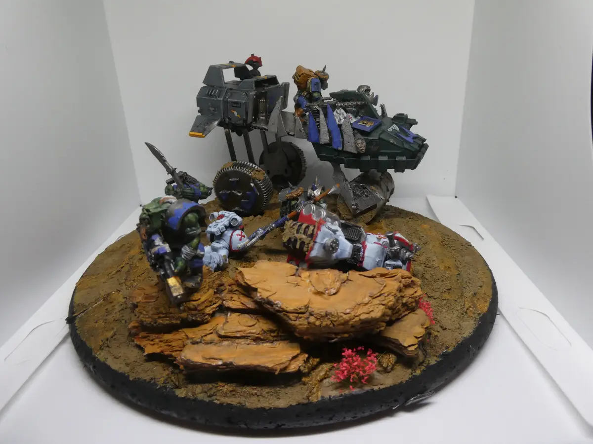 A detailed miniature wargaming diorama featuring painted sci-fi figures and vehicles on a rocky, dirt-covered circular base…