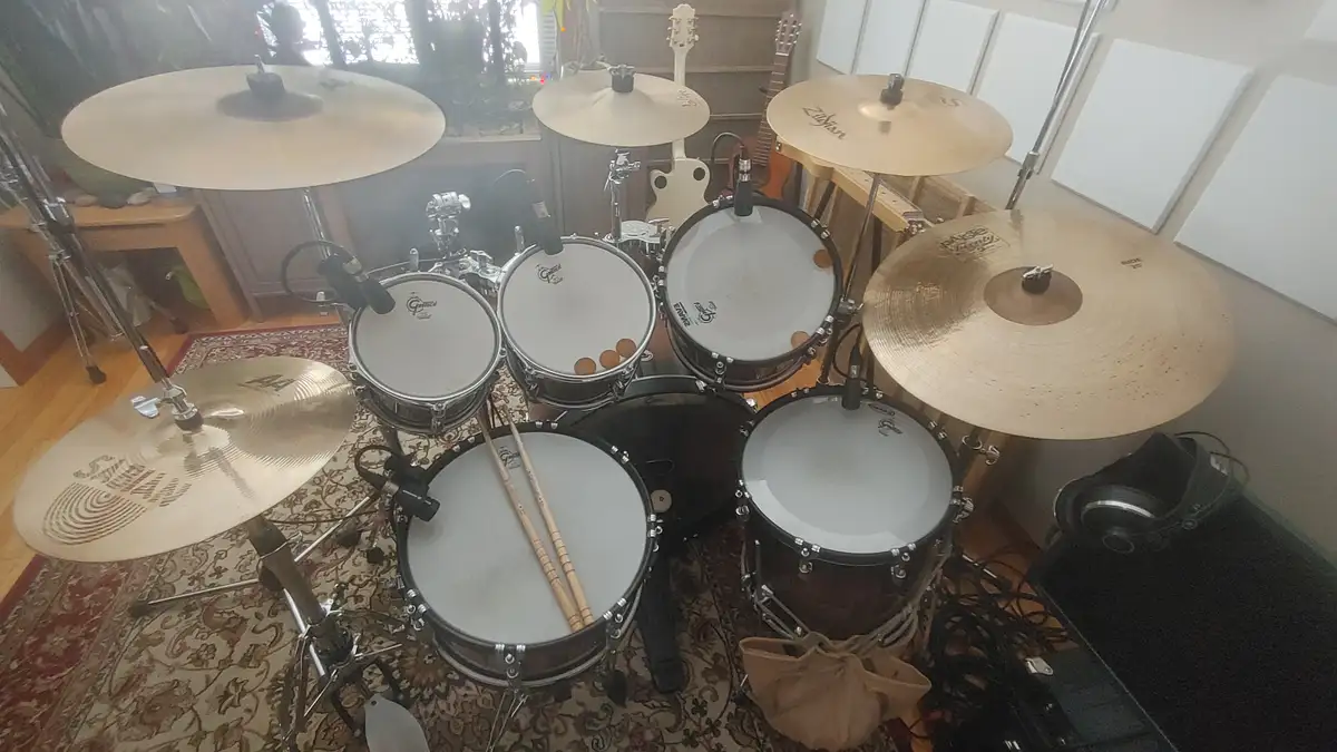 An overhead photo shows a full drum kit with multiple cymbals, drums, and drumsticks resting on the bass drum. The kit is…