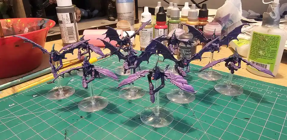 A collection of purple-painted miniature fantasy creatures with bat-like wings and horns, mounted on clear plastic stands…