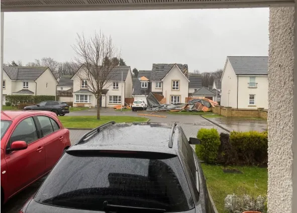 A photo taken from inside a house looking out onto a residential street where several houses have roofs damaged or…