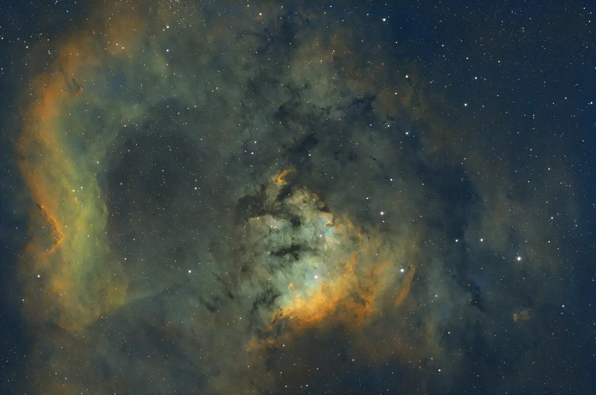 A cosmic image of a colorful nebula with swirling clouds of orange, green, and blue gas against a dark starfield. The…