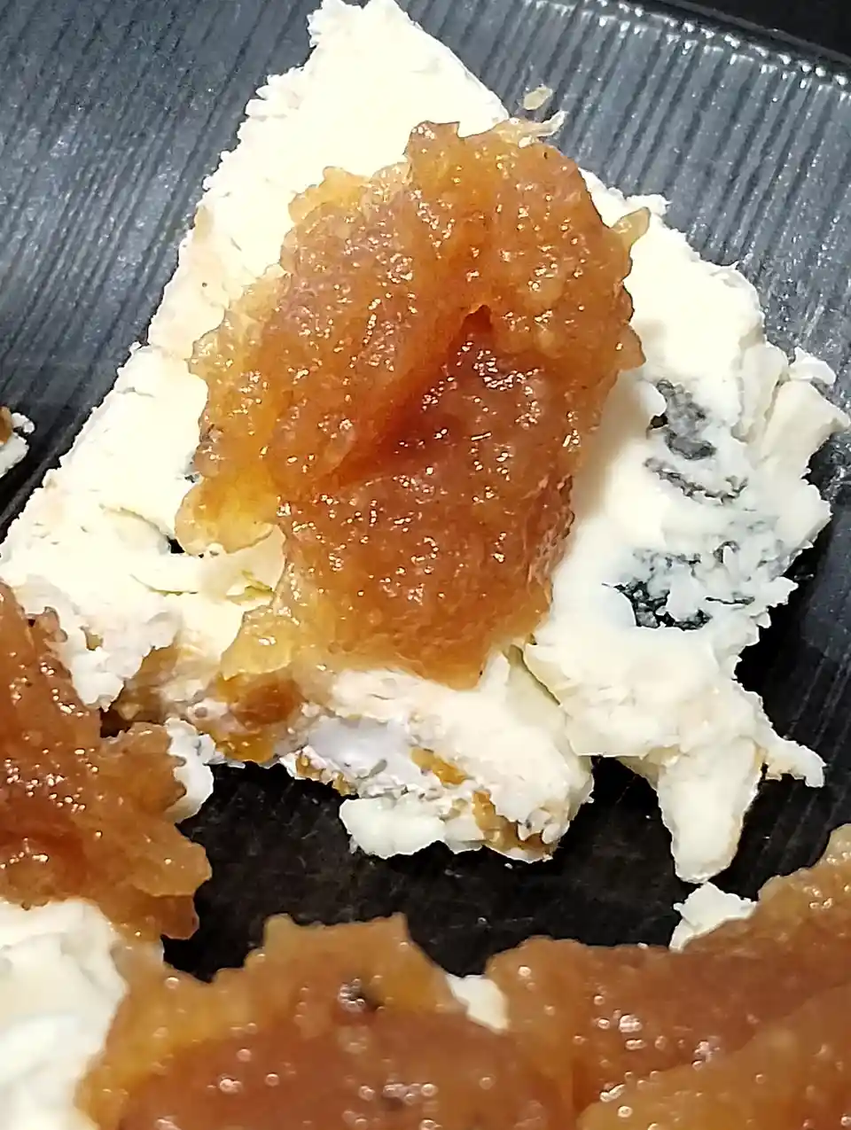 A close-up photo shows a piece of blue cheese with a glossy, amber-colored topping that resembles caviar or fruit preserve…