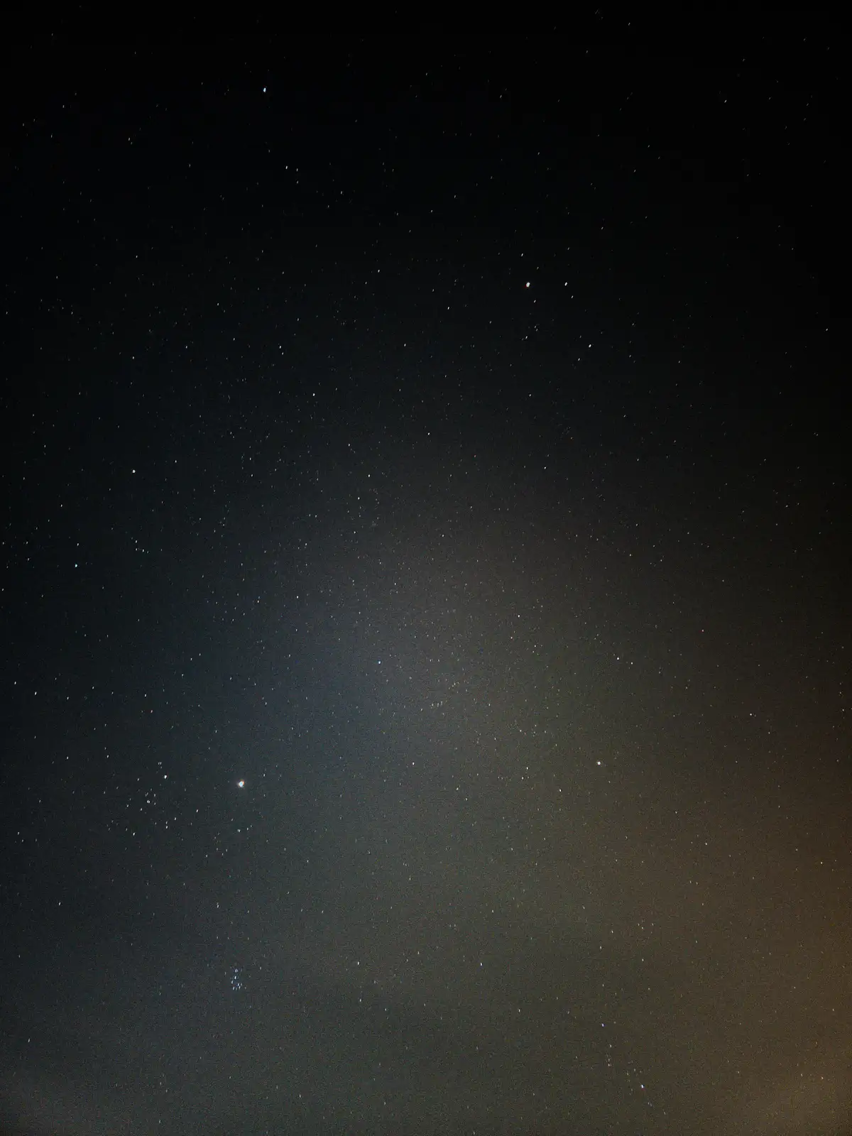 A night sky photograph showing countless stars scattered across a dark expanse, with a noticeable gradient of light…