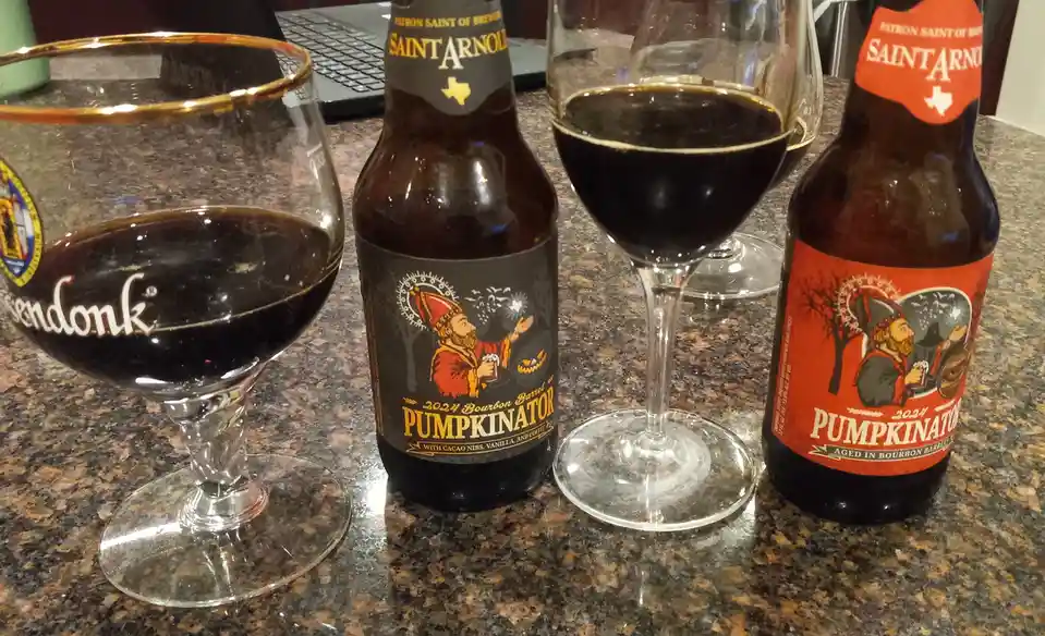 Two bottles of Saint Arnold Pumpkinator beer, one with a black label and one with a red label, sit on a granite countertop…