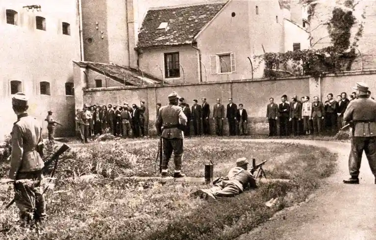 a black-and-white historical photograph shows a group of men in suits standing in a line against a wall, surrounded by…