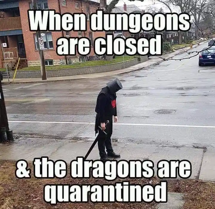 A person dressed in dark fantasy armor with a bucket for a helmet stands dejectedly on a wet city street, holding a sword…