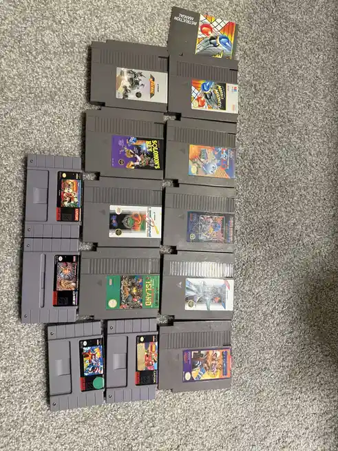 An overhead shot displays a collection of 15 gray Nintendo Entertainment System (NES) game cartridges arranged in a loose…