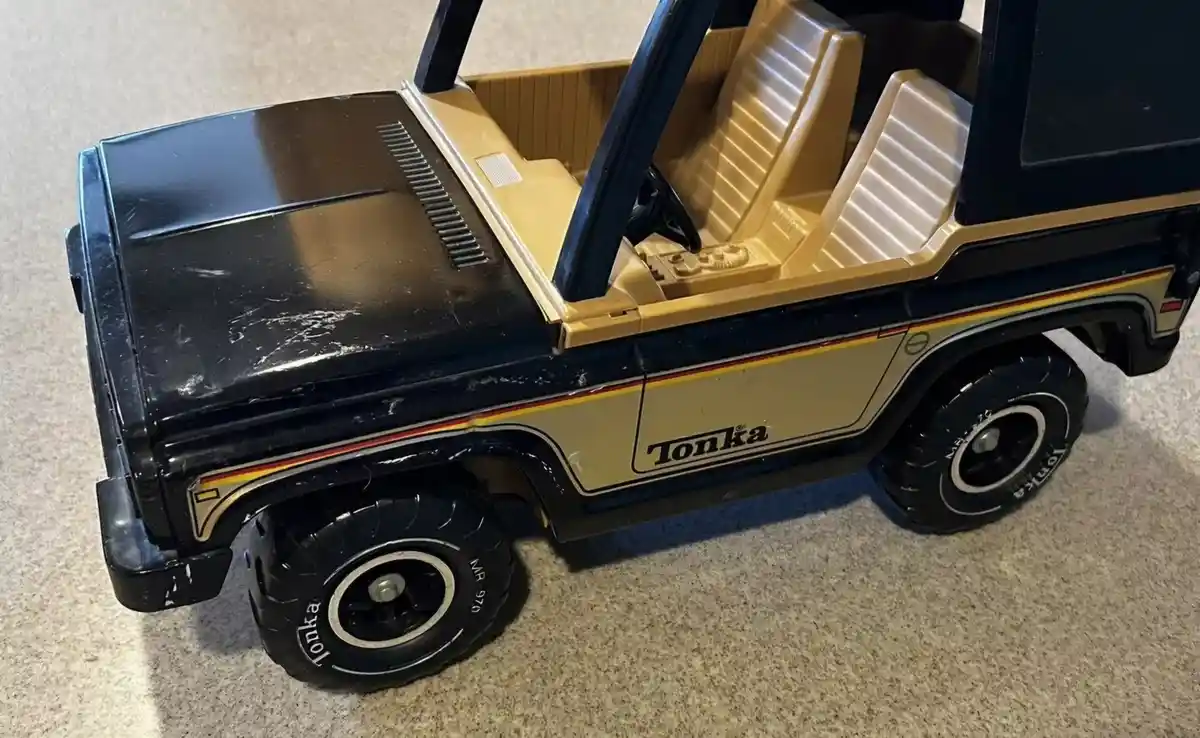 A close-up of a vintage Tonka toy truck, black and beige with orange and yellow stripes, showing its interior and wheels on…
