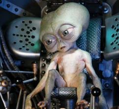 A small, green-skinned alien with large, sad eyes sits in a mechanical cockpit, looking downcast. The image is overlaid with…