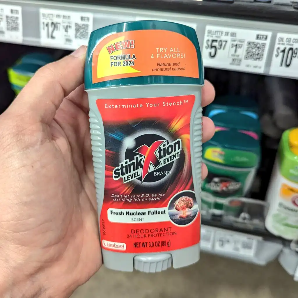 A hand holds a deodorant stick in a store aisle, labeled 'Stink Level Xtion Event Brand' with a 'Fresh Nuclear Fallout'…