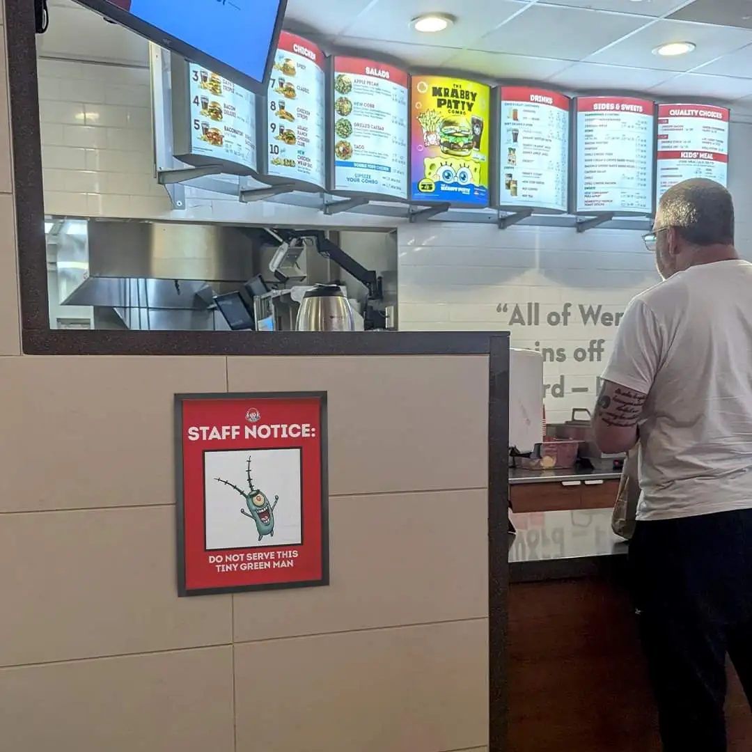 A photo taken inside a fast-food restaurant, likely a Burger King, showing a customer at the counter. Above the counter…