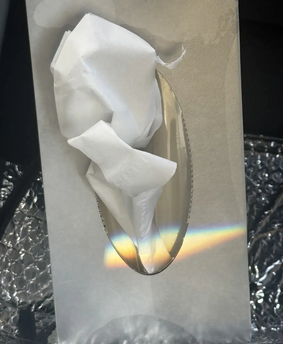 A close-up photo shows a crumpled white tissue partially emerging from an oval-shaped slot in a transparent plastic bag. A…