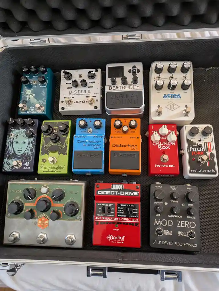 An overhead shot of a hard-shell case filled with various guitar effect pedals from brands like Boss, Radial, and…