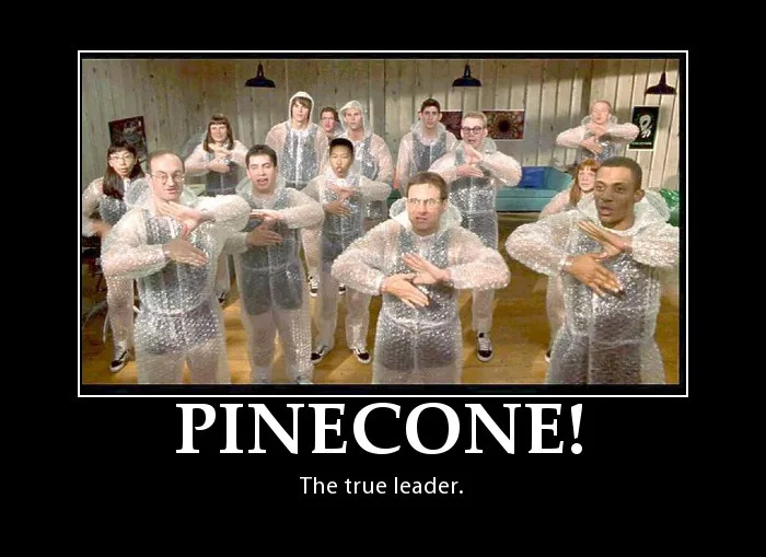 A group of people in clear plastic ponchos are posing in a room, many making a hand gesture with both hands forming a 'T'…