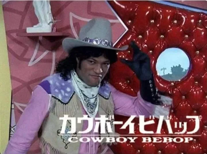 A man in a cowboy hat, pink shirt, and fringed vest poses confidently in front of a red tufted couch. He wears black gloves…