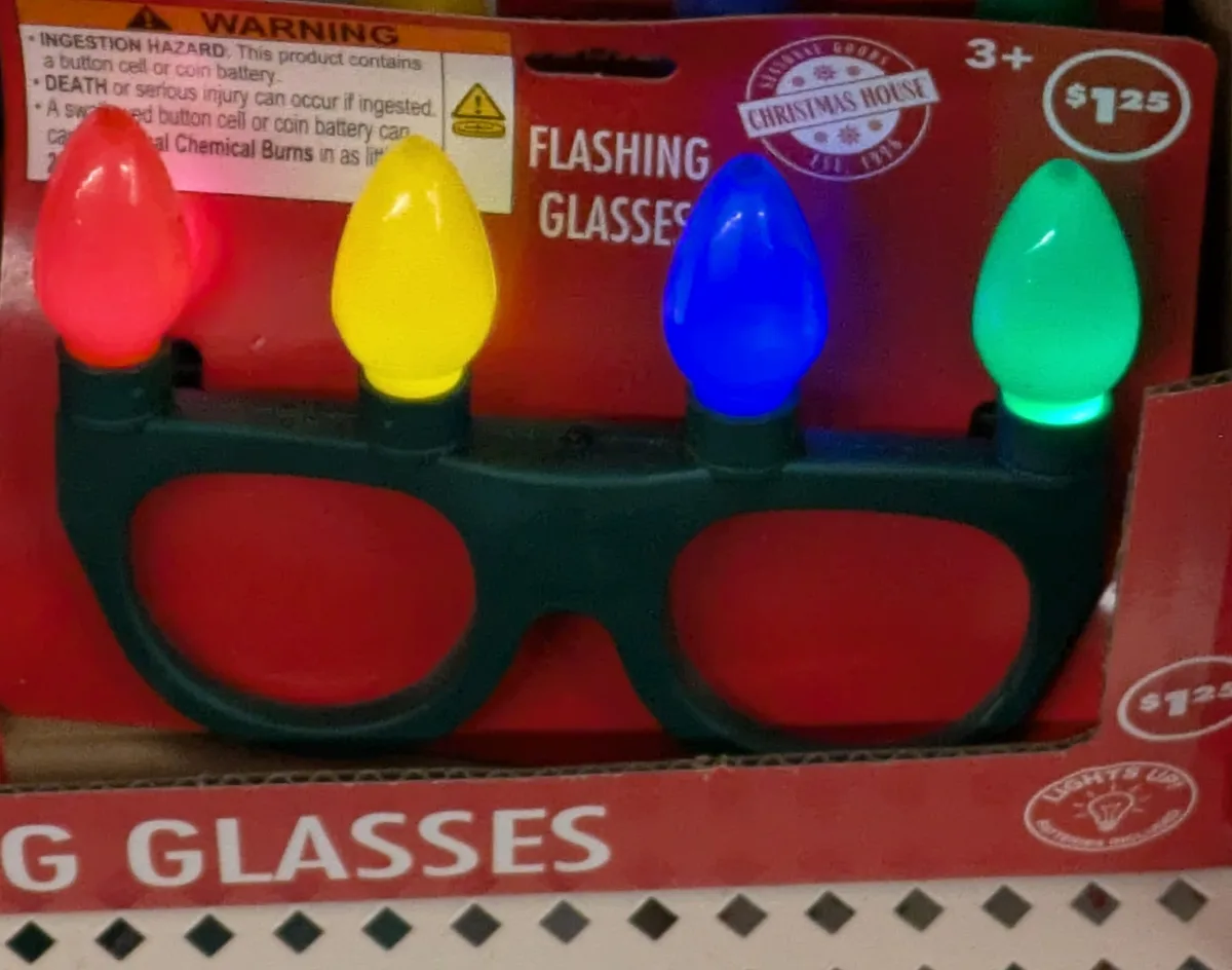 A close-up of a children's toy called 'Flashing Glasses' in its red packaging, featuring four colorful, lit-up bulbs (red…