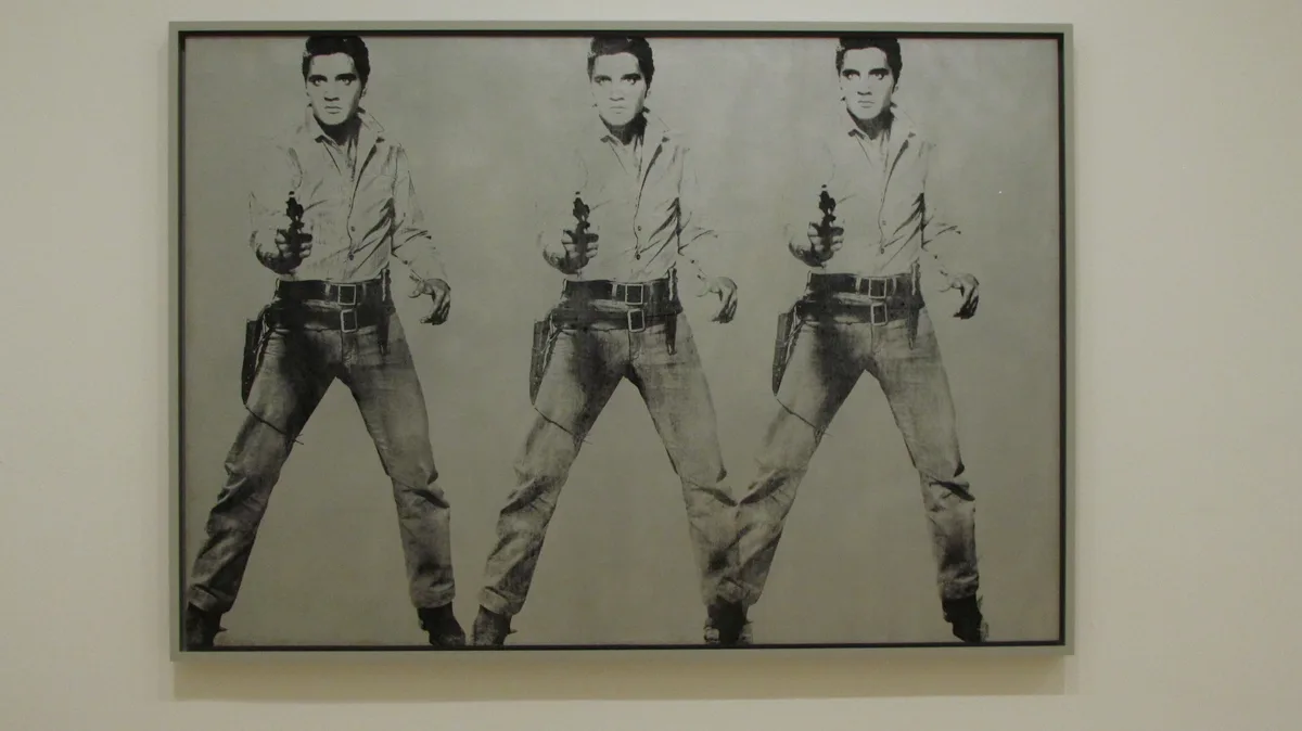A framed black-and-white artwork displays three identical, side-by-side images of Elvis Presley in a dynamic pose, holding a…