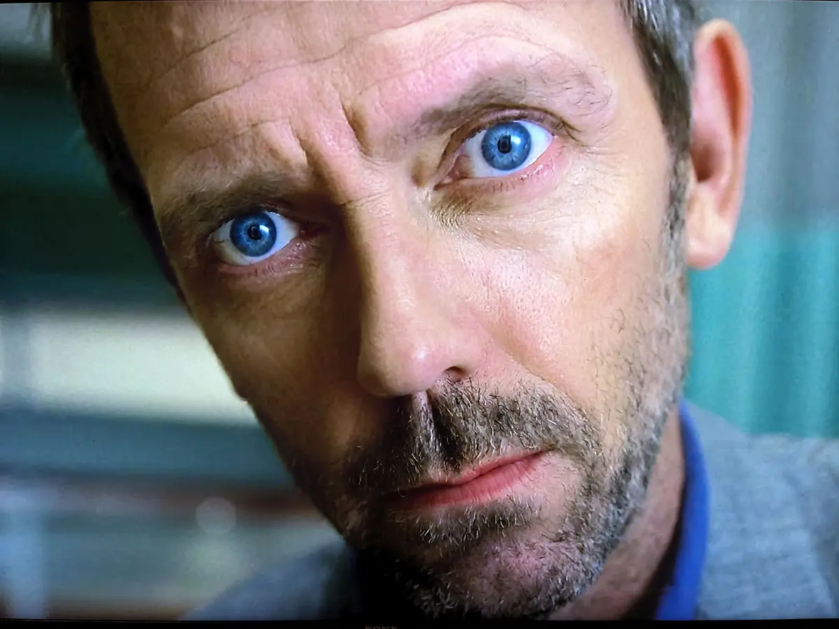 A close-up shot of actor Hugh Laurie as Dr. Gregory House from the TV show 'House, M.D.', showing his intense blue eyes and…