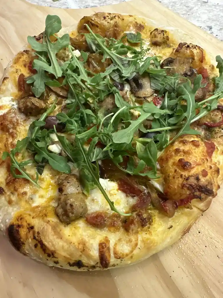 A close-up photo of a freshly baked pizza with a golden-brown crust, topped with melted cheese, sausage, mushrooms, olives…