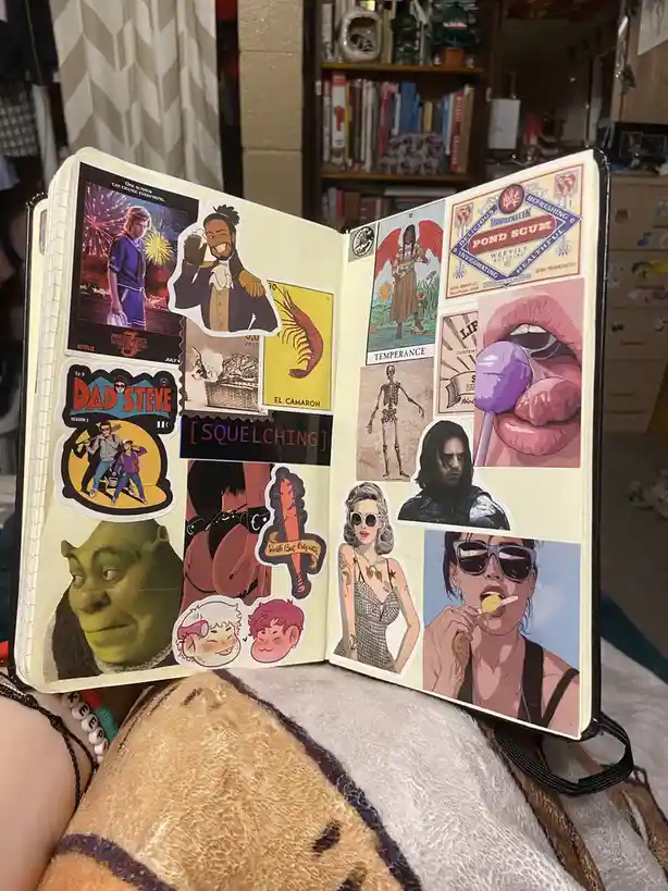 An open scrapbook or journal page covered in a dense collage of colorful stickers featuring diverse pop culture imagery…