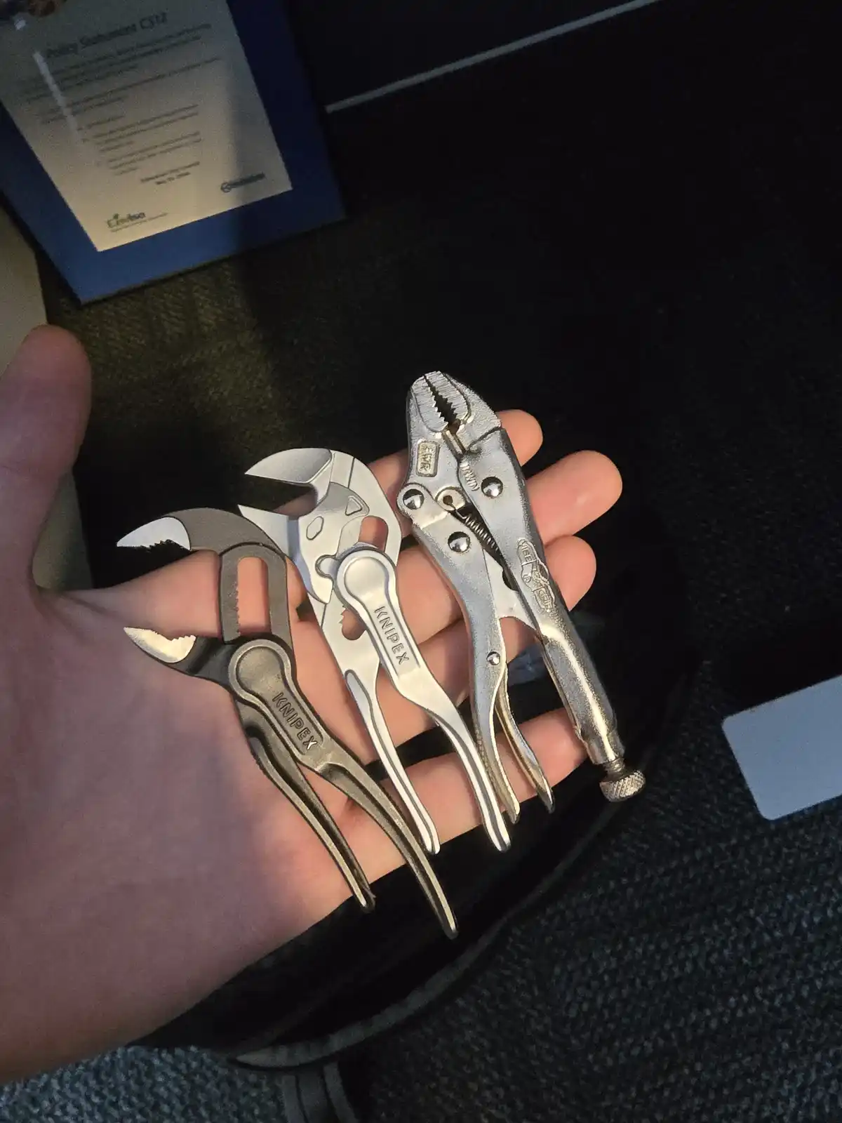 A hand holds three small, silver-colored Knipex brand pliers of varying types, including adjustable and locking pliers…