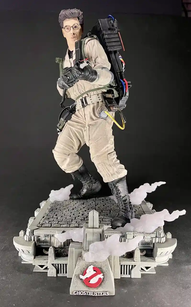 A detailed Ghostbusters action figure of the character Egon Spengler, wearing his signature beige jumpsuit, glasses, and…