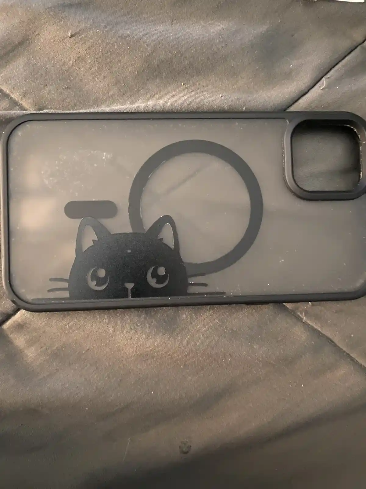 A transparent phone case with a black cat silhouette design, where the cat's head peeks out from behind a circular cutout…