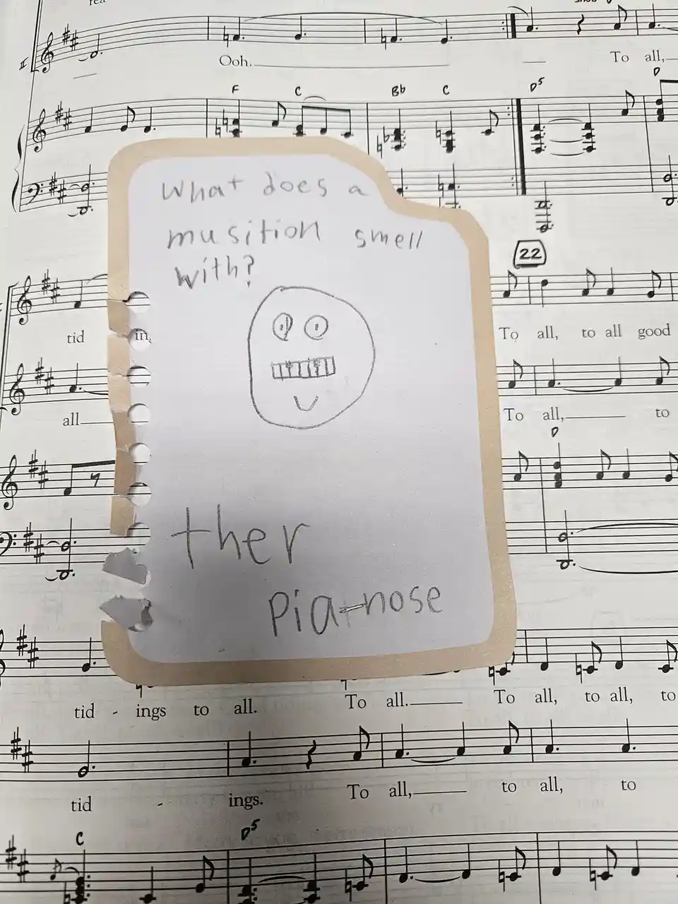 A handwritten note on torn paper, taped over sheet music, asks 'What does a musician smell with?' and answers 'ther…