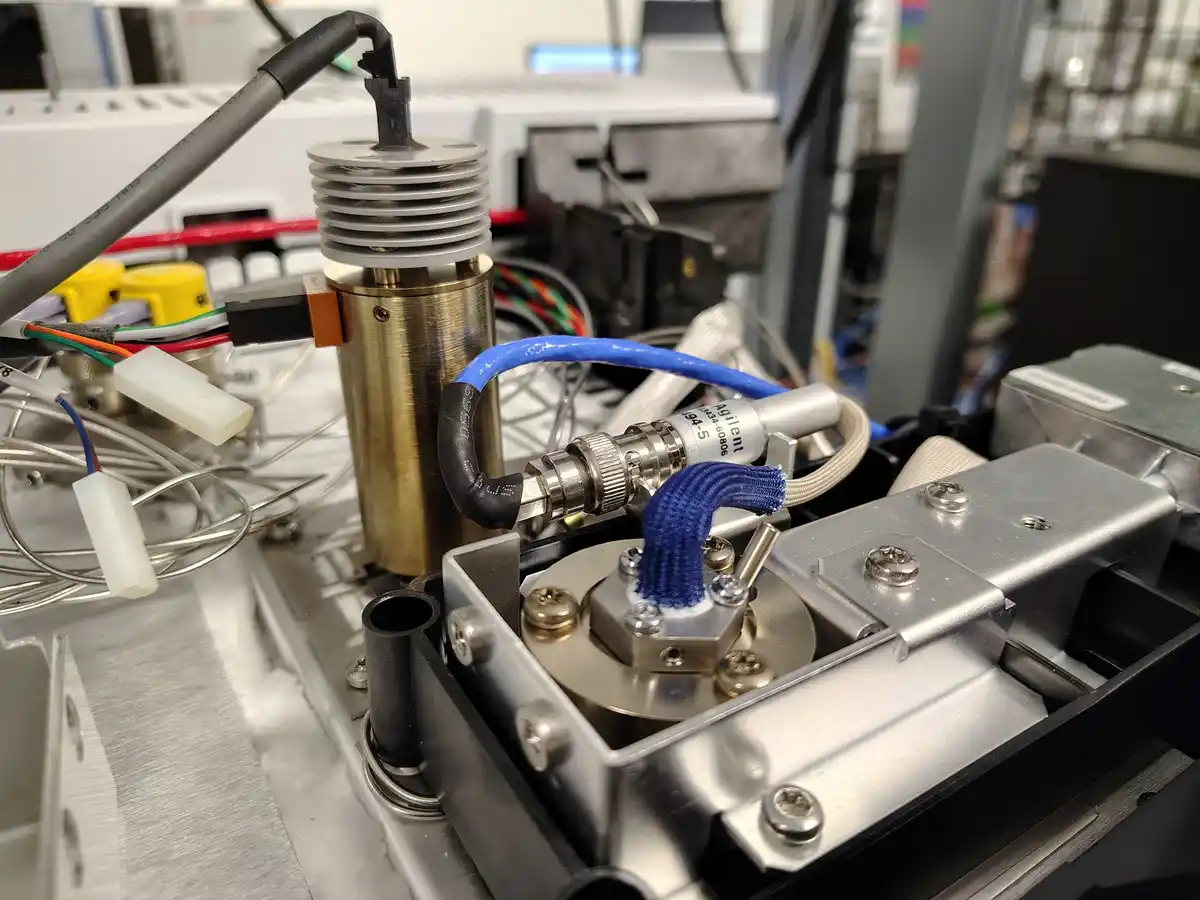 A close-up photo of complex laboratory equipment, including a brass cylinder, various wires, and an Agilent branded…