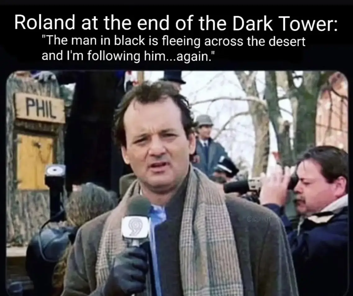 A man with dark hair and a plaid scarf holds a microphone with a '9' logo while speaking, surrounded by people and…
