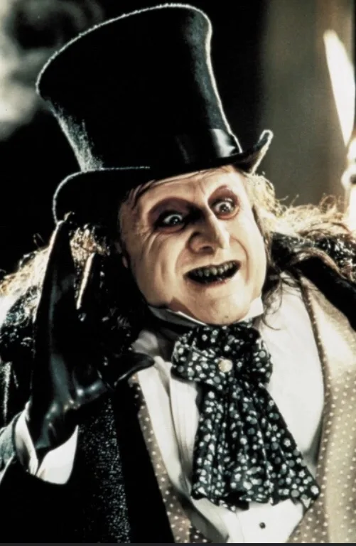 A close-up of the character known as the Penguin from the 1990 film 'Batman Returns', wearing a tall black top hat, a white…