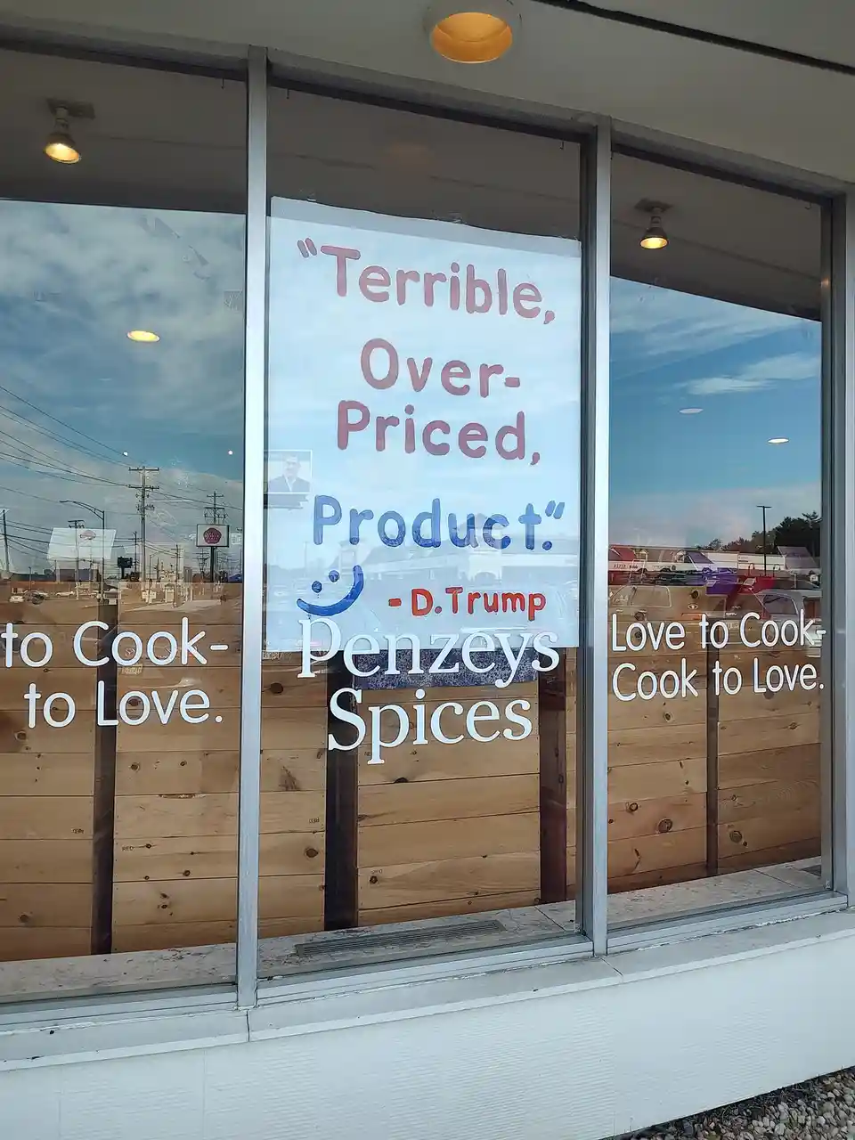 A storefront window of Penzeys Spices displays a handmade sign with a sarcastic quote attributed to 'D.Trump' that reads…
