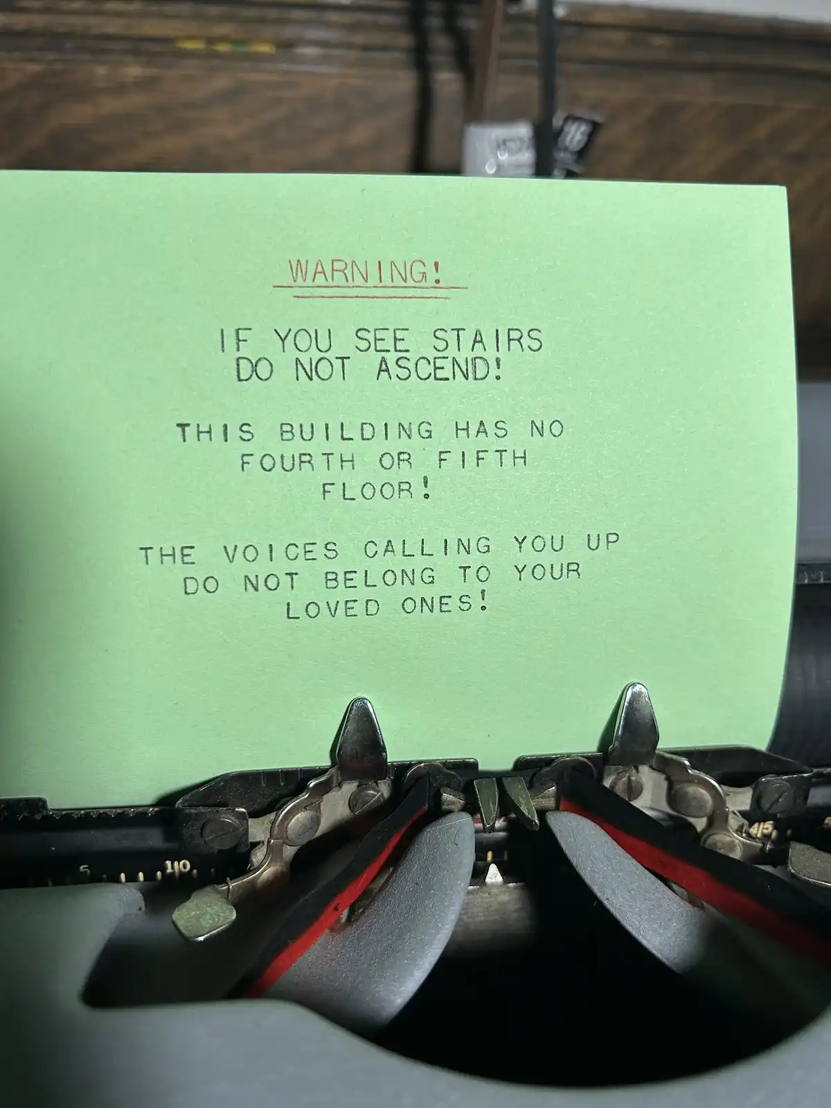 A close-up photo of a green sheet of paper typed on a vintage typewriter, displaying a warning message that humorously…
