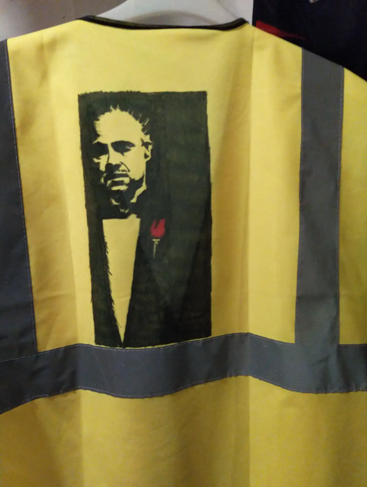 A yellow high-visibility safety vest with black reflective stripes has a printed graphic of a man in a tuxedo with a red…