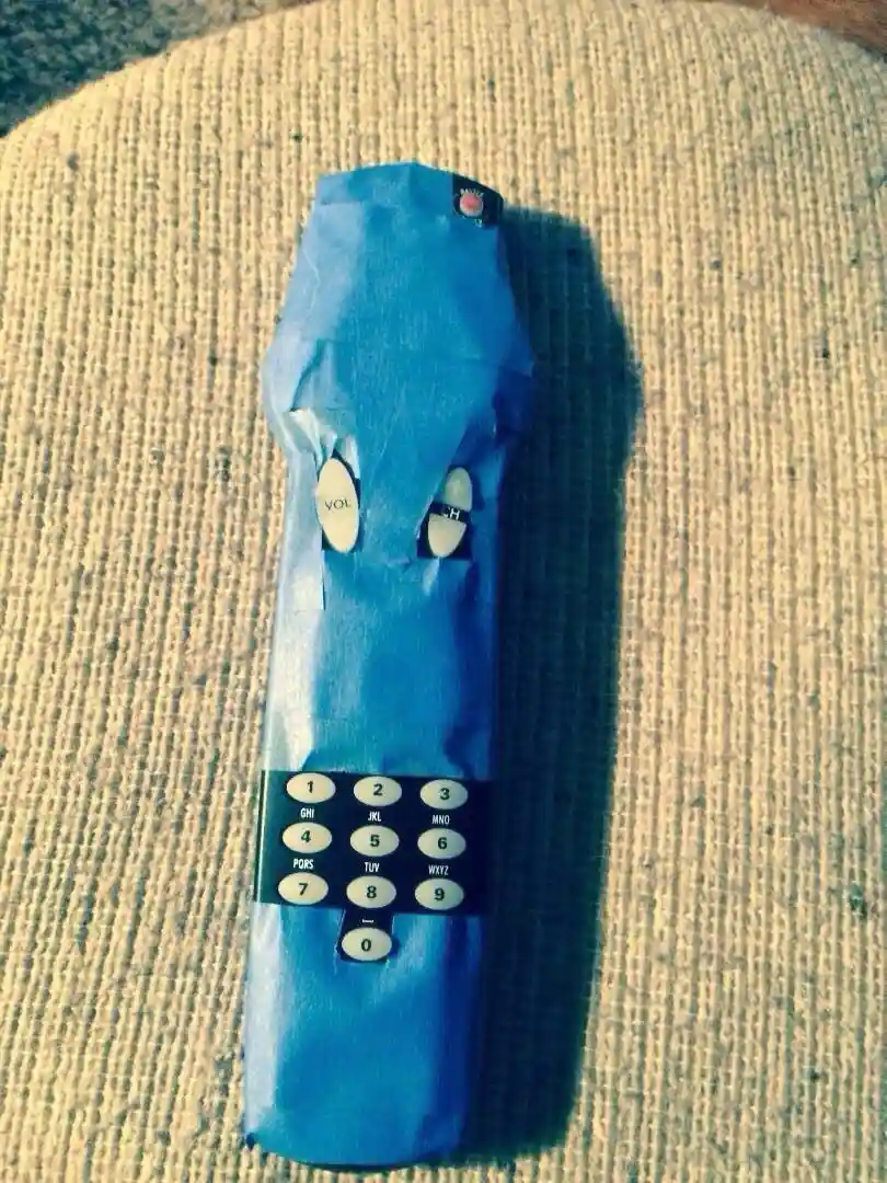 A blue TV remote control is wrapped in blue duct tape, with only the volume and channel buttons visible through cutouts…