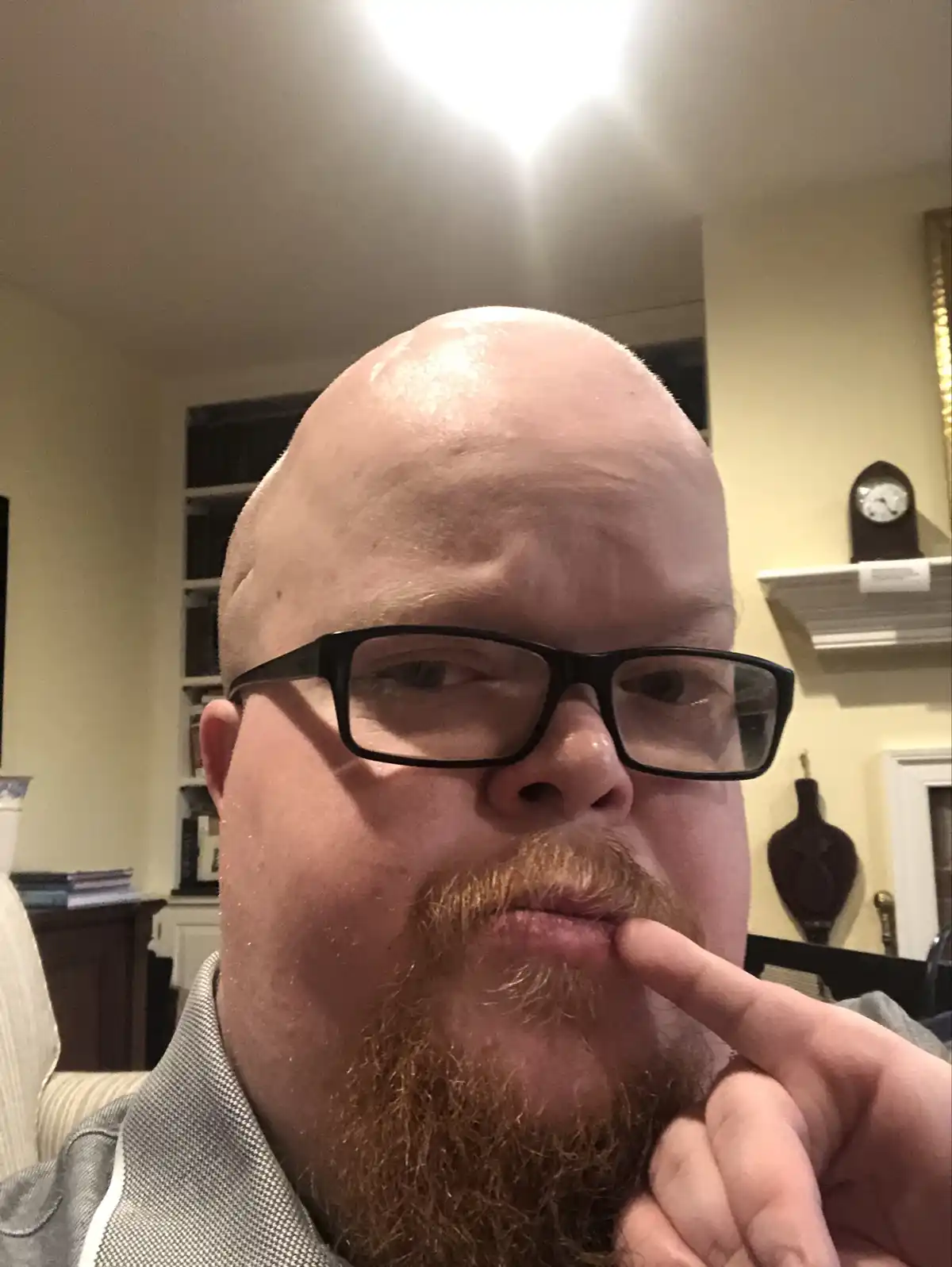 A close-up selfie of a bald man with a full reddish beard and black-rimmed glasses, looking directly at the camera while his…