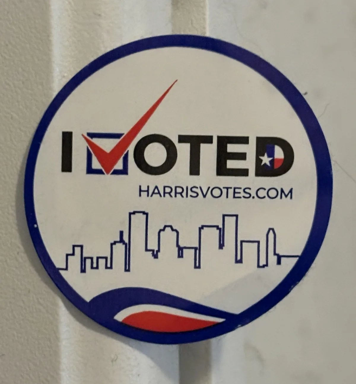 A circular 'I VOTED' sticker from Harris County, Texas, featuring a red checkmark replacing the 'V', a Texas flag replacing…