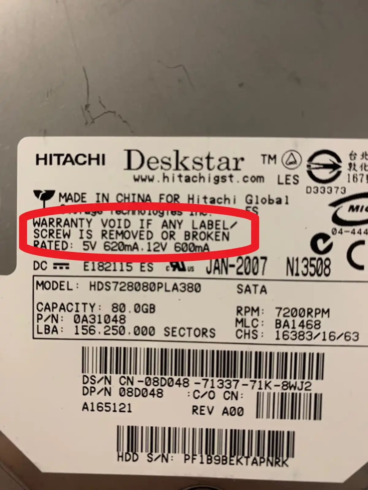 A close-up photo of a Hitachi Deskstar hard drive label with a red circle highlighting the warranty disclaimer text that…